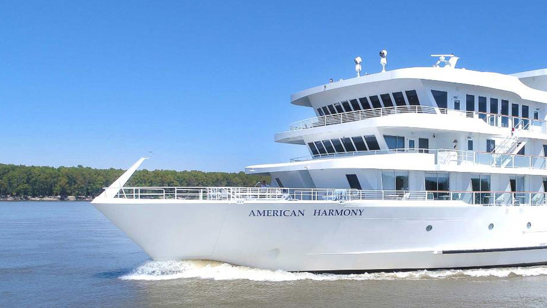 Bow of the riverboat American Harmony cruising a tree-lined river